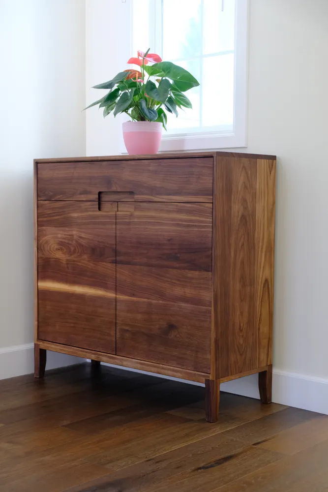 Walnut cabinet with a potted plant on top, in a sunlit corner