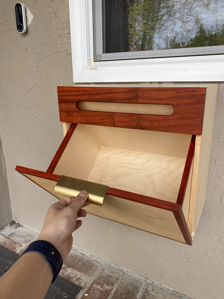 A hand pulling open the mailbox's drop-front compartment